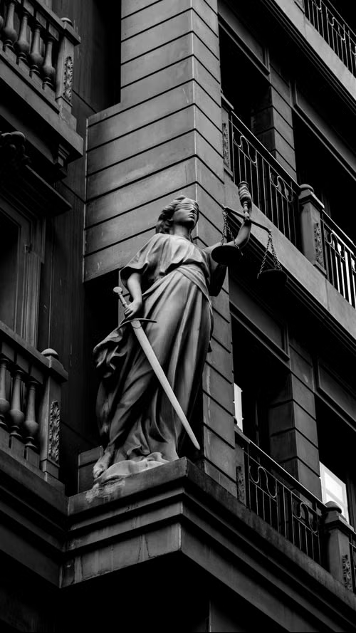 Escultura da Dama da Justiça com balança e espada em fachada clássica, em preto e branco